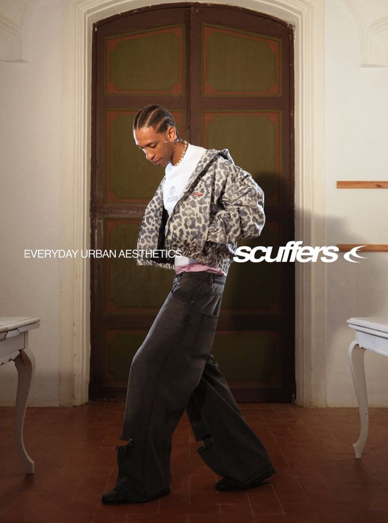 A person in a leopard print jacket and distressed wide-leg jeans poses in front of a dark wood door with white trim in an indoor setting.