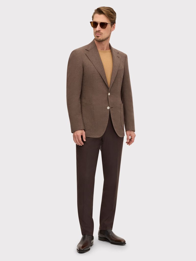 Full-length shot of an adult male model in a brown suit and sunglasses posing against a white background in a fashion style photo.