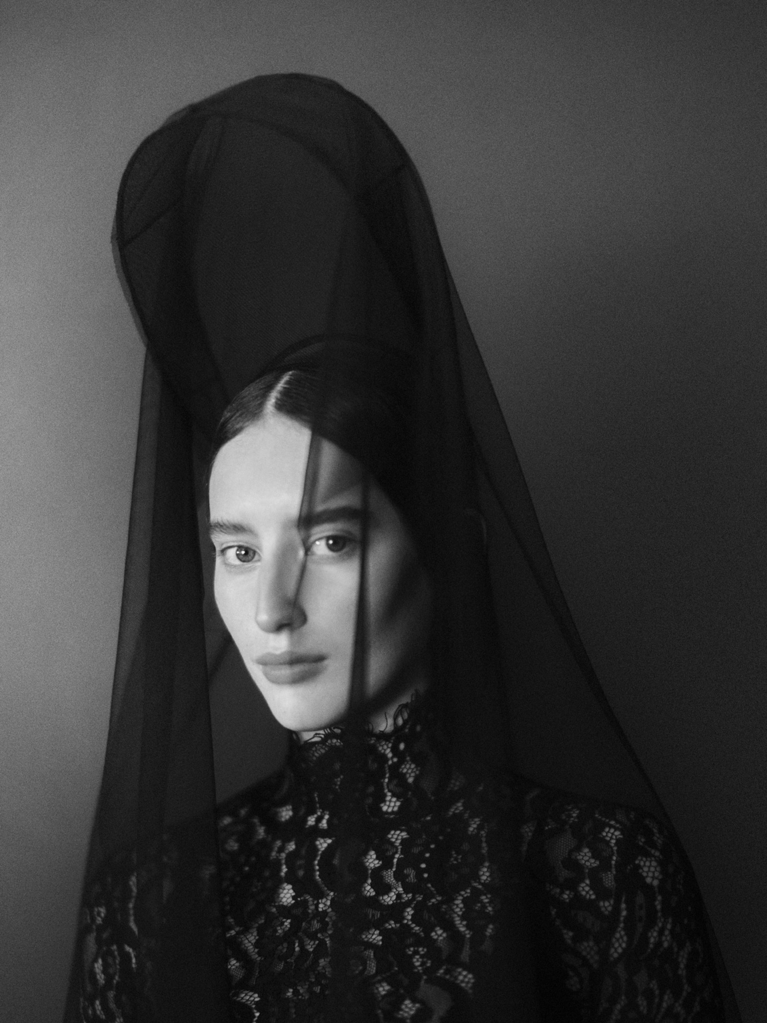 Striking black and white portrait of a fair-skinned woman with dark hair, wearing a lace top and draped in sheer black veil.