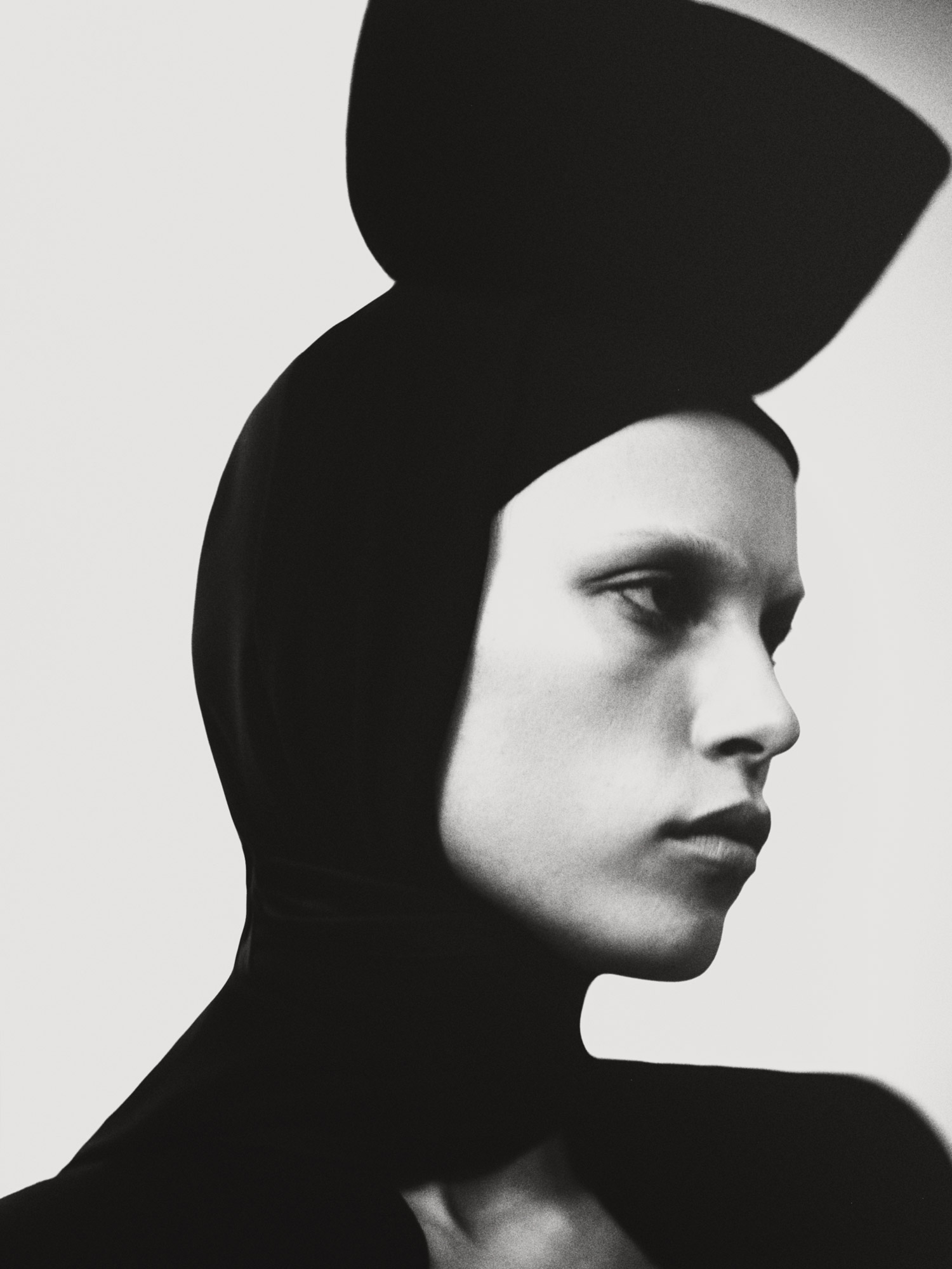 Monochrome portrait of an adult woman in a black head covering. The model is facing left, with an expressionless gaze.