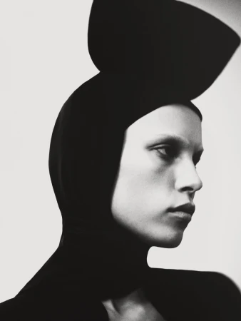 Monochrome portrait of an adult woman in a black head covering. The model is facing left, with an expressionless gaze.