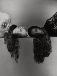 Two models lying head to head with long flowing hair against a neutral studio backdrop in a black and white editorial portrait