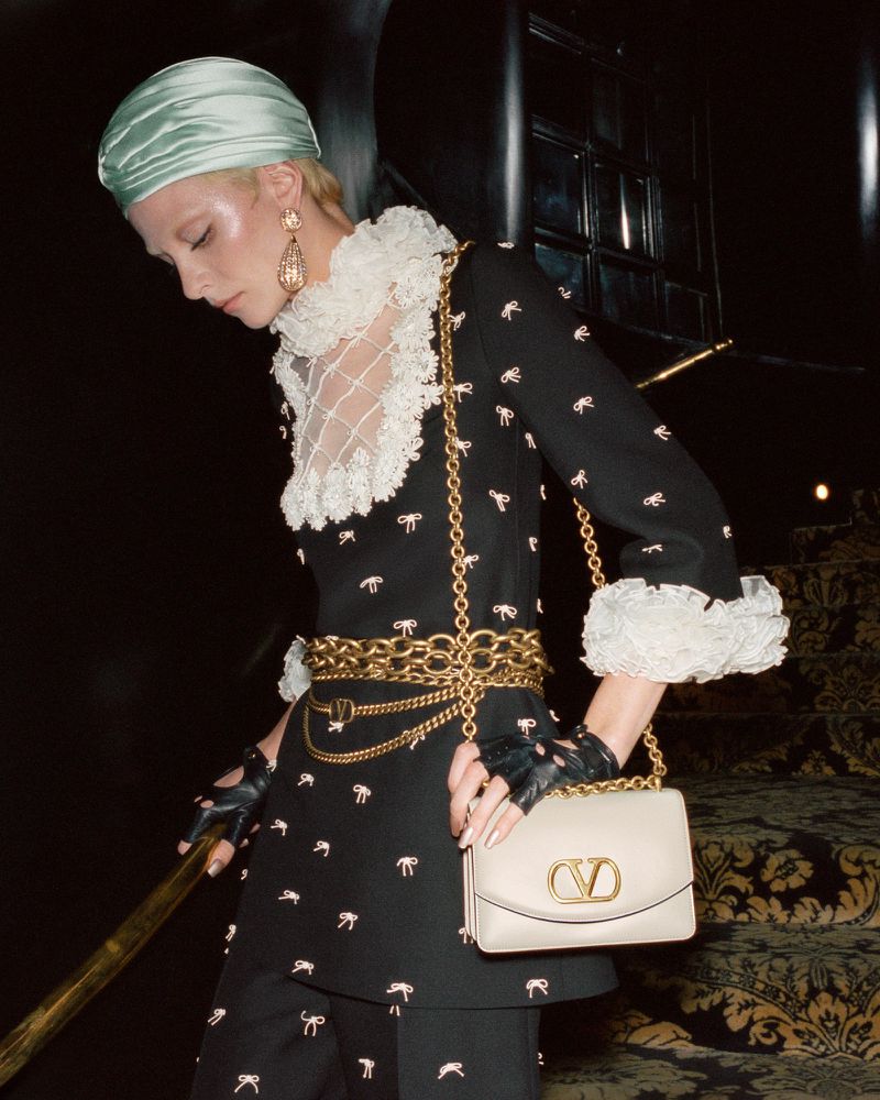 Fashionable woman in black and white dress with cream purse and gold jewelry on stairs, modeling dark academia aesthetic.