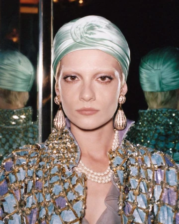 Model wearing pale green satin turban and embellished blue jacket with drop earrings reflected in mirrors