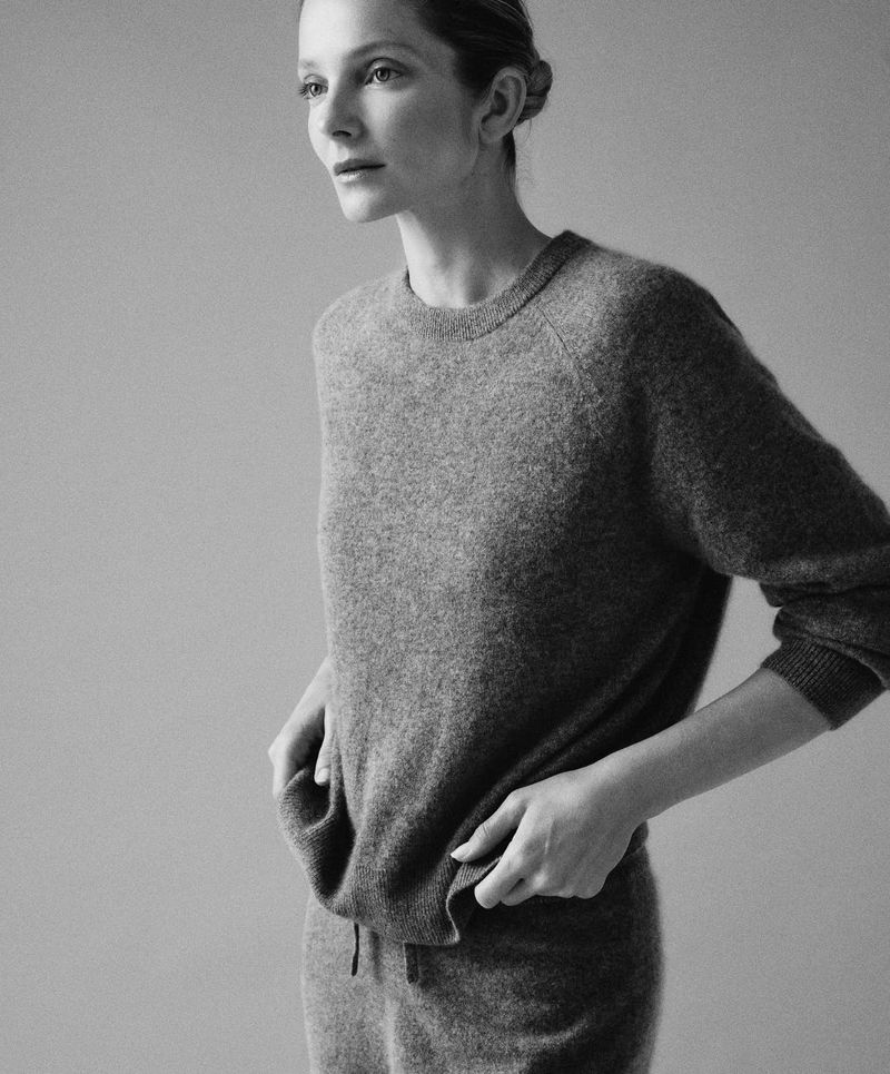 Monochrome portrait of a woman wearing a grey knit sweater and sweatpants against a neutral background in a fashion editorial.