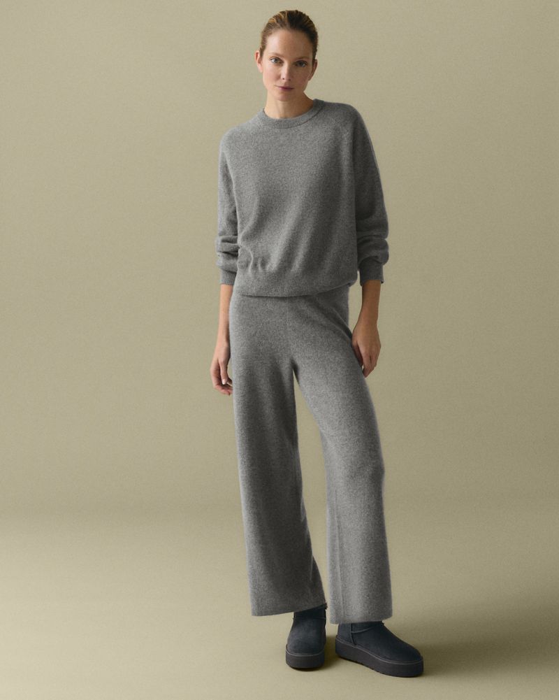 A woman models a grey lounge set with a crew neck sweater and wide-leg pants, paired with black platform shoes in a studio setting.