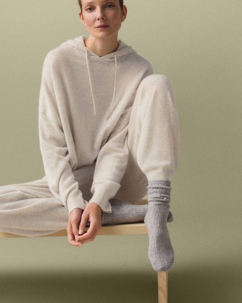 Model Eniko Mihalik sitting on a stool wearing a cream cashmere hoodie and matching trousers for Oysho