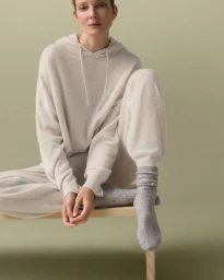 Model Eniko Mihalik sitting on a stool wearing a cream cashmere hoodie and matching trousers for Oysho