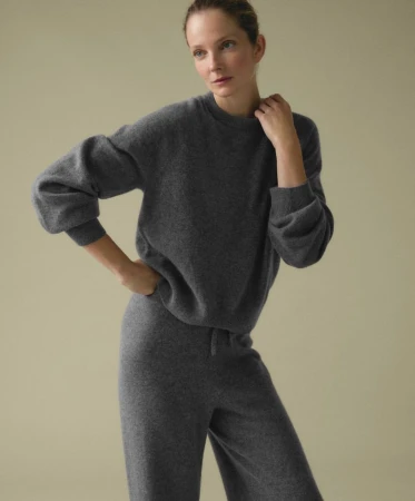 Model wearing a grey cashmere crewneck sweater and matching trousers against a plain studio background.
