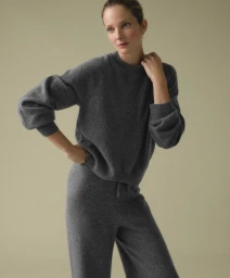 Model wearing a grey cashmere crewneck sweater and matching trousers against a plain studio background.