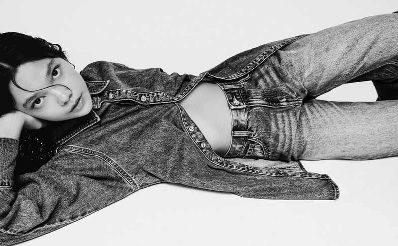 Model lying on side wearing a denim shirt and jeans against a plain white background for Bershka DENIM.