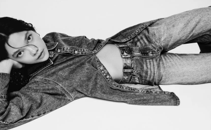 Model lying on side wearing a denim shirt and jeans against a plain white background for Bershka DENIM.