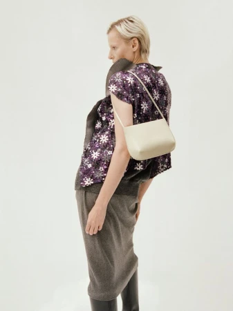 Model wearing a patterned purple floral top and grey skirt carrying a light handbag against a white background