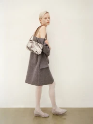 Model in grey coat and white tights holding a patterned shoulder bag against a plain background