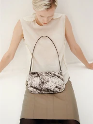 Model in cream sleeveless top and skirt holding a printed shoulder bag against a plain white background