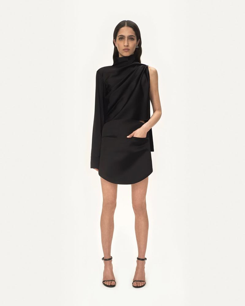 Model wearing a black asymmetric mini dress and strappy heels against a white seamless background for Courreges