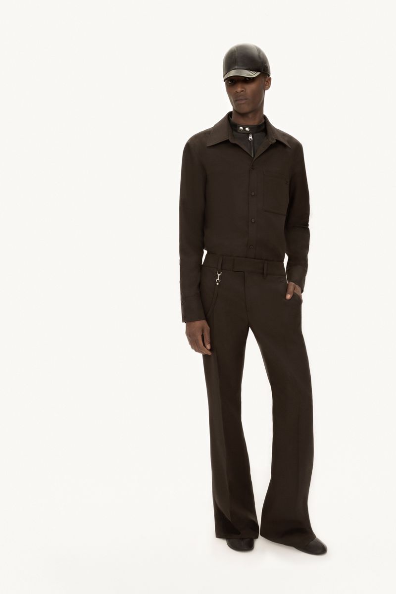 Dark-skinned male model in brown monochrome outfit and leather cap posing in photo studio with soft light on a white backdrop.