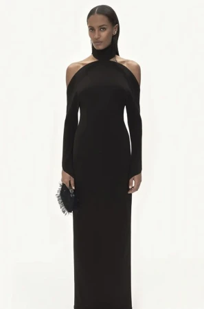 Model wearing a black cold shoulder long dress holding a dark fringed handbag against a plain white background