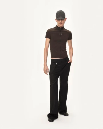Model wearing a brown fitted zip shirt and black trousers with a grey cap against a white background