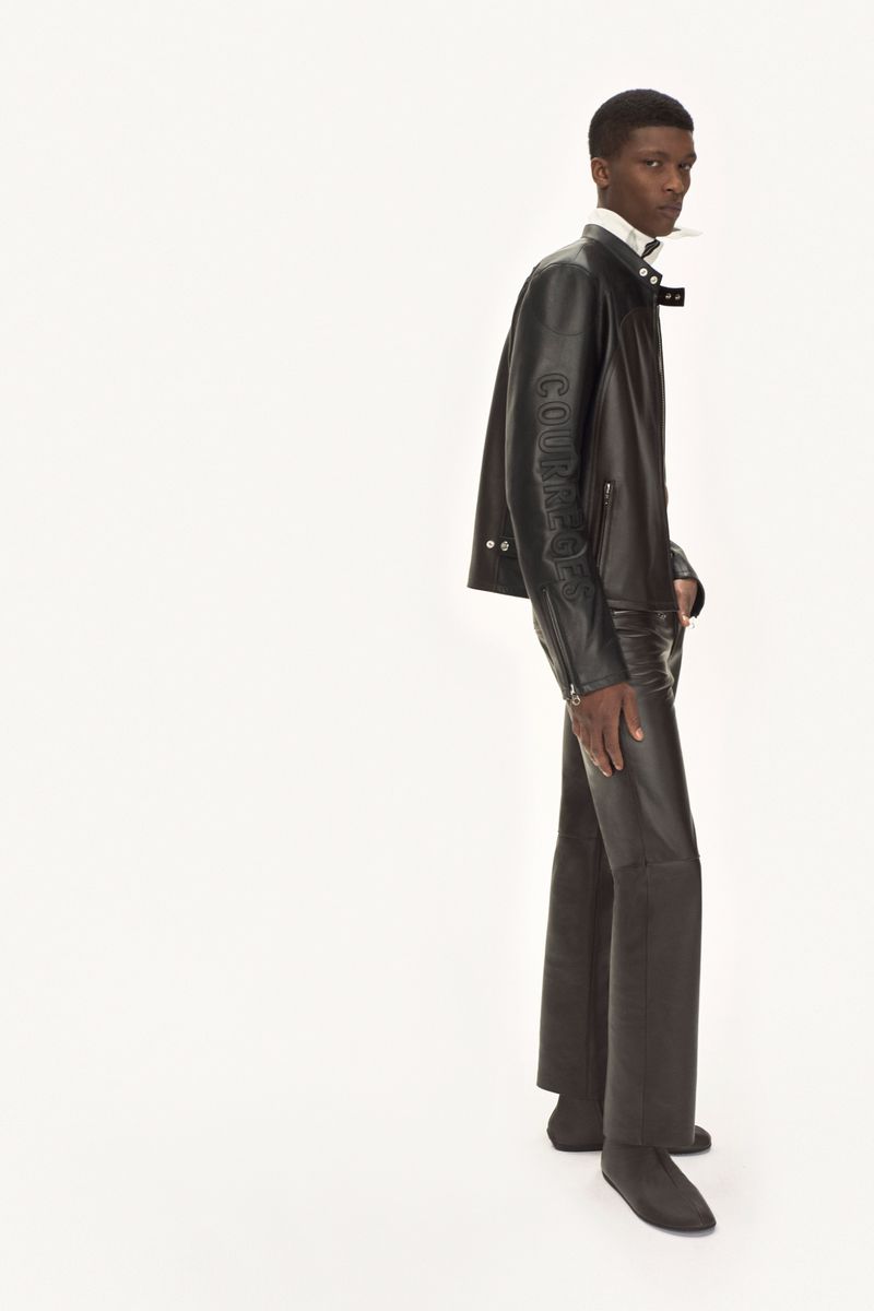 Full-length studio shot of an adult male wearing a brown leather jacket and matching brown leather trousers against a white background.