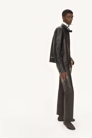 Full-length studio shot of an adult male wearing a brown leather jacket and matching brown leather trousers against a white background.