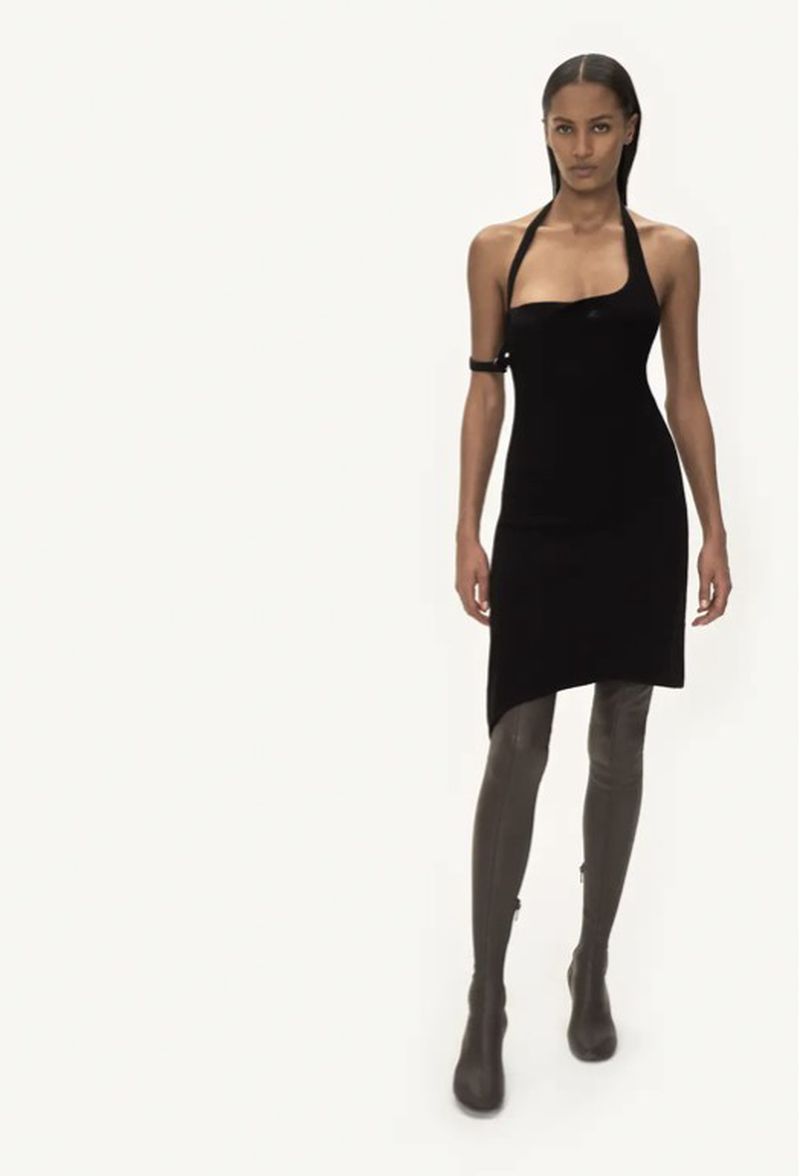 Runway fashion: A female model walks in a black halter dress and thigh-high boots against a stark white background, showcasing a minimalist aesthetic.