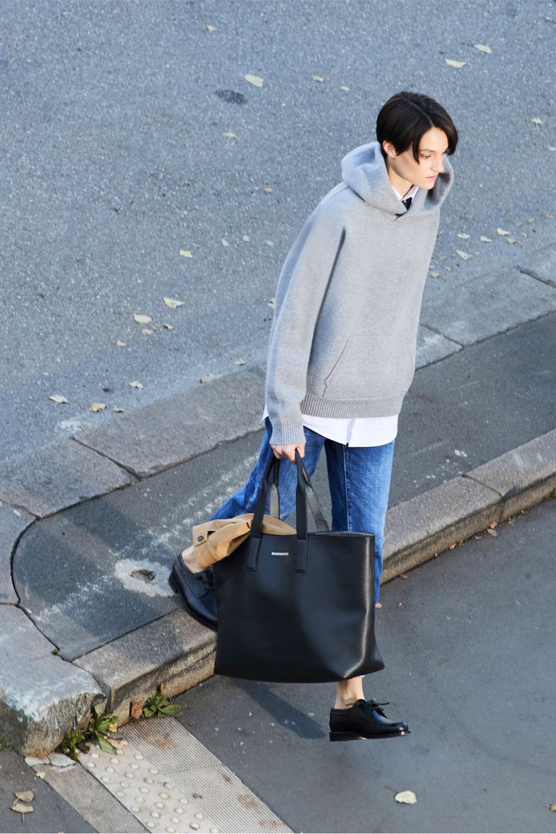 Woman in gray hoodie and jeans walks on the street, holding a black tote bag in daylight, captured from a high angle view.