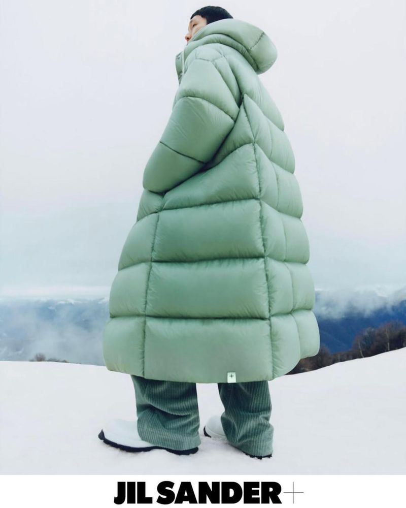 Adult posing outdoors in a puffy light-green hooded coat, light-green pants, and white boots, standing in a snowy environment.