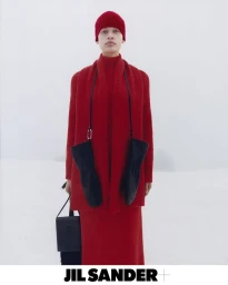 Model standing outdoors in a snowy landscape wearing a monochromatic red knit beanie, sweater, scarf, skirt, and holding black leather gloves