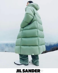 Model in a long quilted sage green puffer coat and matching trousers standing on a snowfield