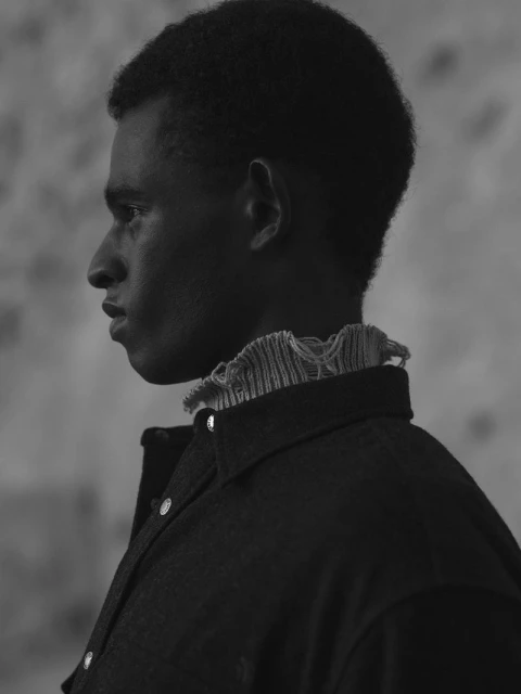 Monochrome portrait of a young adult male in profile wearing a collared shirt with ruffled trim against a mottled background.
