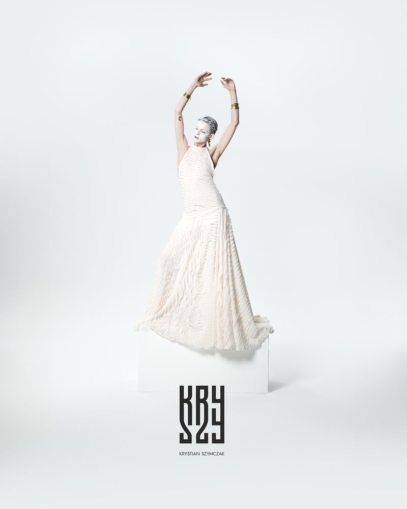 A striking fashion shot features a woman in a white dress posing on a cube, with her arms raised against a bright, clean background.