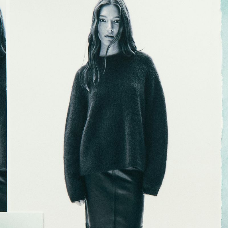 Studio shot of a female model in a dark grey fuzzy sweater and black skirt, posing against a white backdrop with soft lighting.