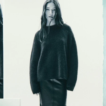 Studio shot of a female model in a dark grey fuzzy sweater and black skirt, posing against a white backdrop with soft lighting.