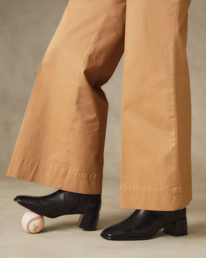 Tan, wide-leg pants paired with black, heeled ankle boots. A baseball is positioned under the toe of one boot in the studio.