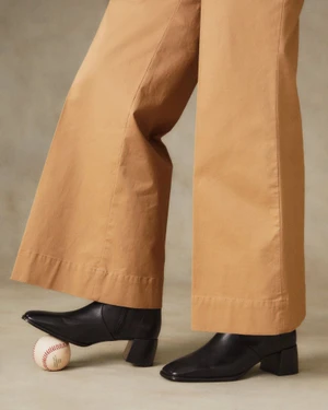 Close-up of camel trousers and black leather boots resting on a baseball against a neutral studio background for Gant FW24.