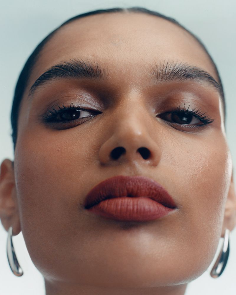 Extreme close-up portrait of a woman wearing dark lipstick and silver hoop earrings against a light background.
