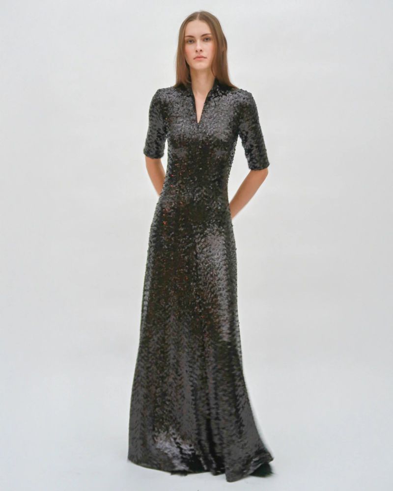 Elegant woman in a shimmering, floor-length gown with short sleeves, posing in a bright studio with soft lighting.