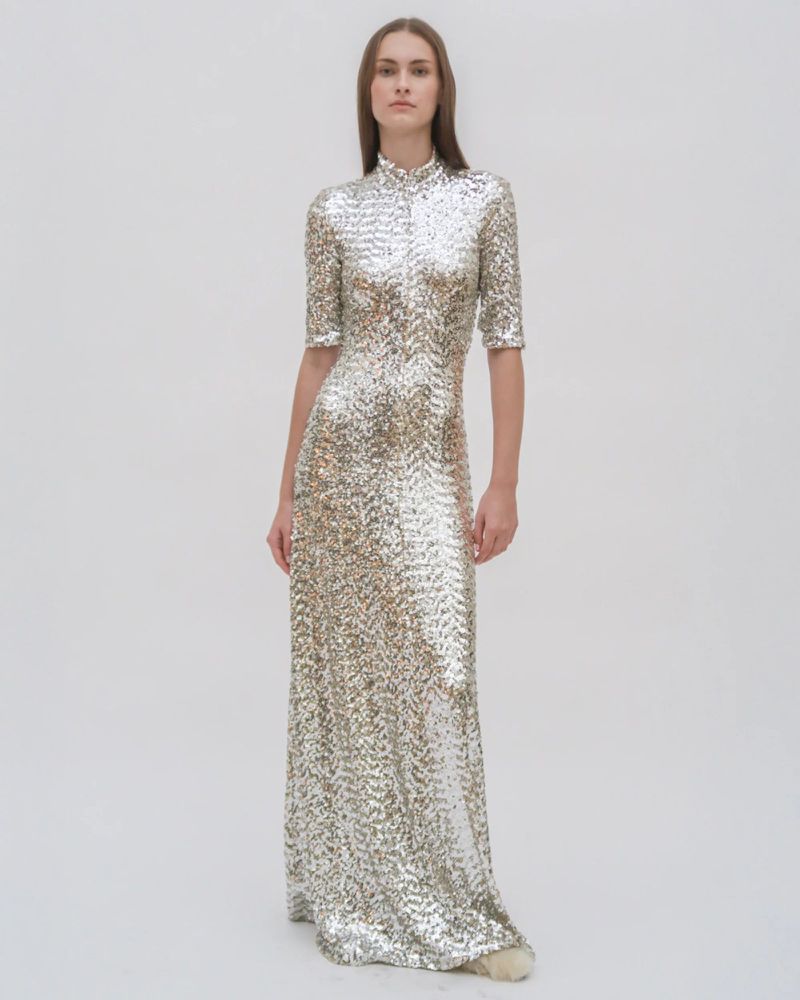 Woman in a floor-length gown with sequins and short sleeves, posing in a bright white, neutral studio setting, fashion photography.