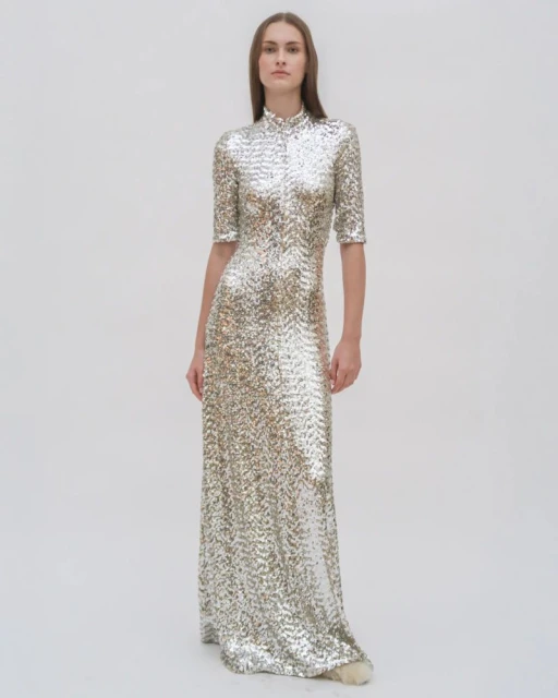 Woman in a floor-length gown with sequins and short sleeves, posing in a bright white, neutral studio setting, fashion photography.