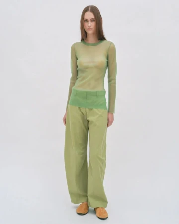 Model standing against a plain white background wearing a sheer green long-sleeve top and matching green trousers.