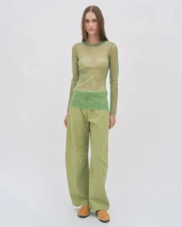 Model standing against a plain white background wearing a sheer green long-sleeve top and matching green trousers.