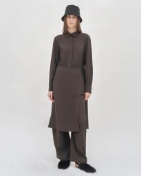 Model in a brown shirt dress and trousers wearing a black bucket hat against a plain white studio backdrop