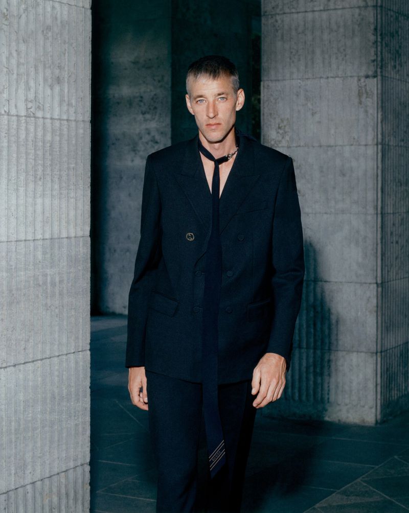 Model Joel Frampton wearing a black double-breasted suit standing between concrete columns in an editorial photograph by Yannick Schuette.