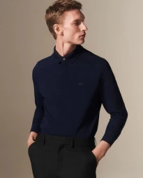 A male model wearing a dark navy polo shirt and black trousers against a neutral studio background.
