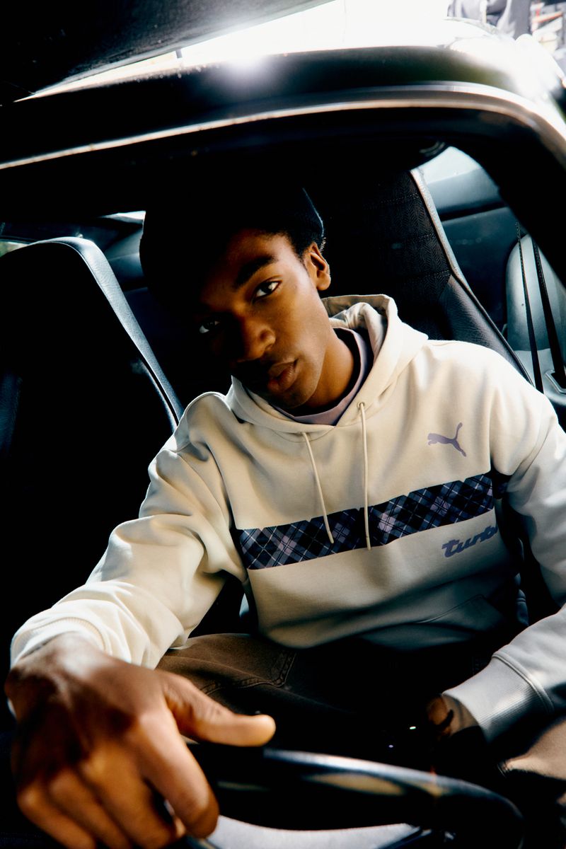 Young man driving a car, wearing a Puma hoodie. Car interior is black, driver looking at the camera.
