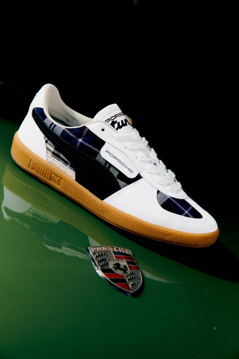 Puma x Porsche trainers on a green surface with the Porsche emblem in an eye-level, medium studio shot with dark background.