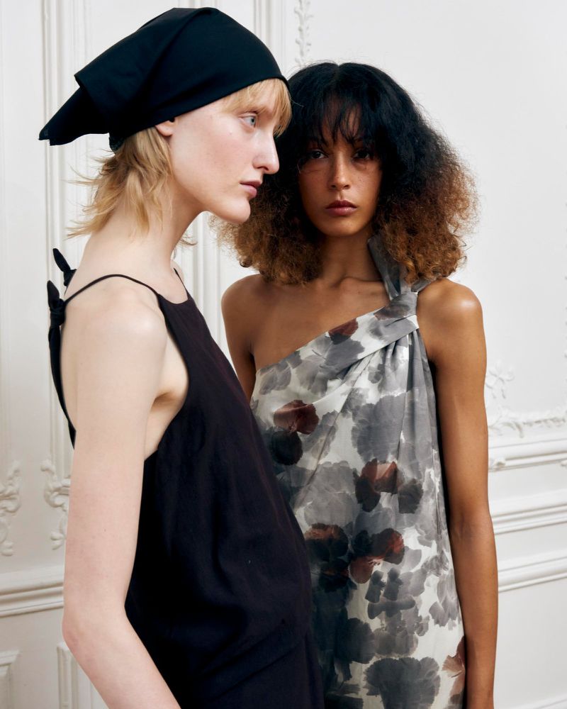 Two female models posing in profile and facing forward against an ornate white interior wall for Christian Wijnants spring summer 25.