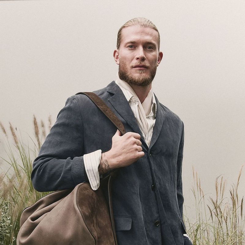 Man with blonde hair and beard wearing a dark blazer holding a brown leather duffel bag for Boss S/S 25
