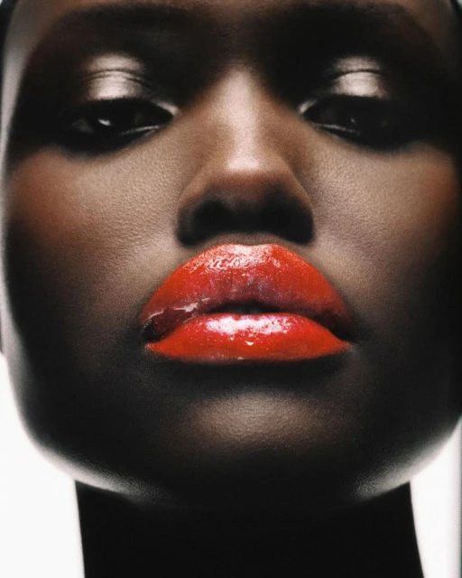 Close-up portrait of a woman with dark skin and shiny red lipstick, capturing a modern beauty aesthetic with professional studio lighting.